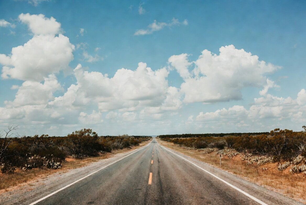 An open highway stretching toward the horizon through flat Texas ranchland — the drive south to the Valley